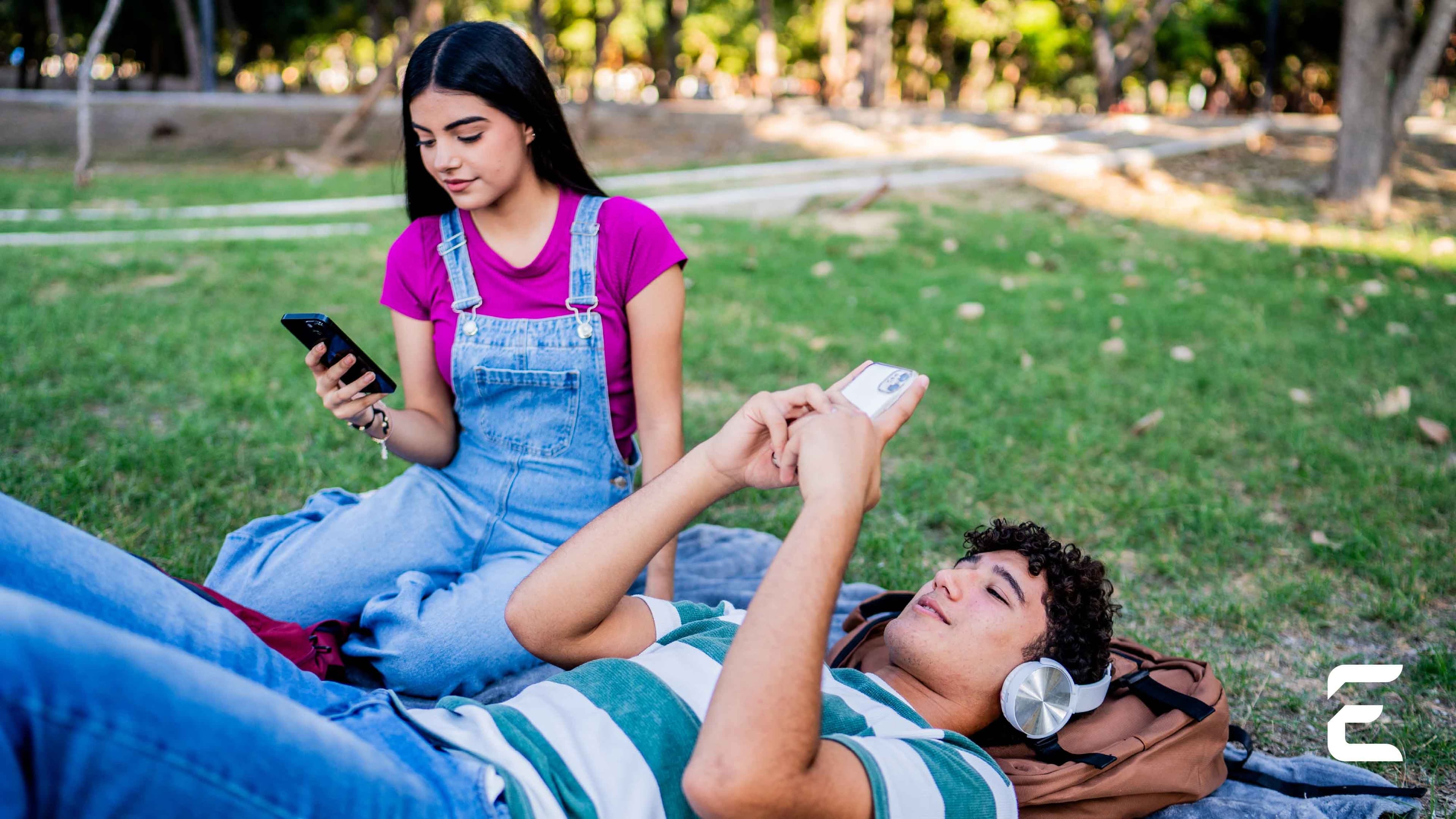 Two young people on grass, engrossed in their smartphones.
