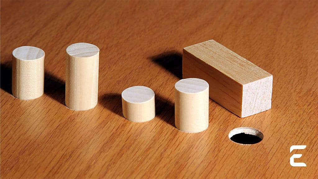 Wooden cylinders and a rectangular block on a wooden surface with a circular hole.