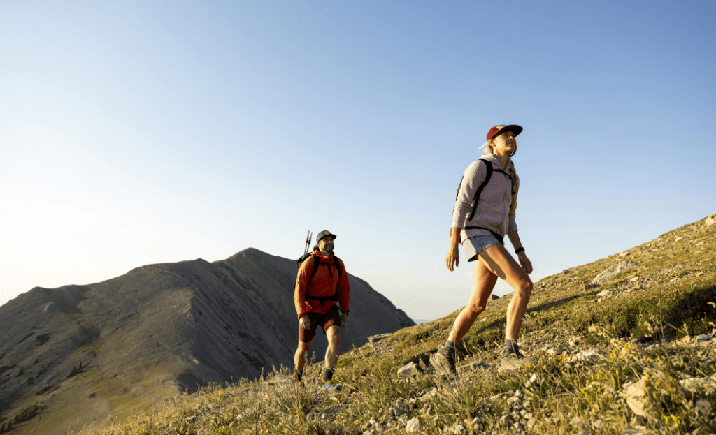 Two people hike up a grassy mountain under a clear sky.
