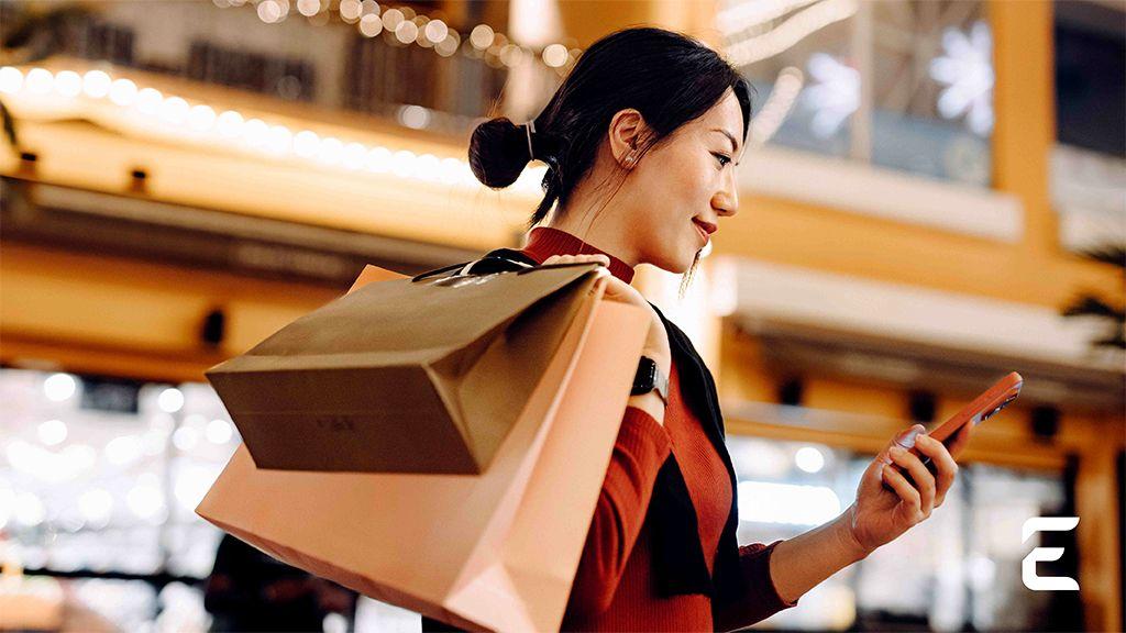 Smiling woman with shopping bags looks at her phone at night.