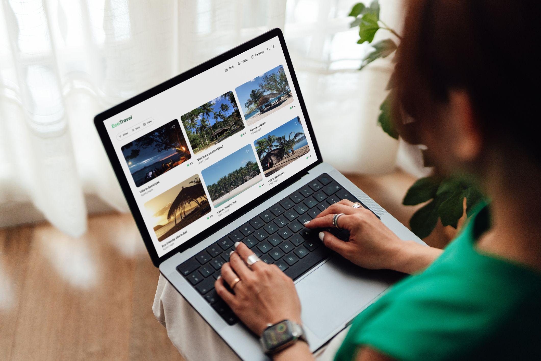 A person types on a laptop displaying the EcoTravel website with tropical travel destinations.