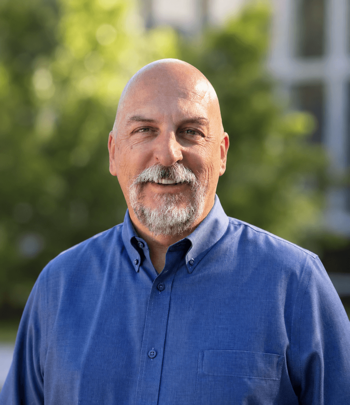 A smiling bald man with a gray beard wearing a blue shirt.