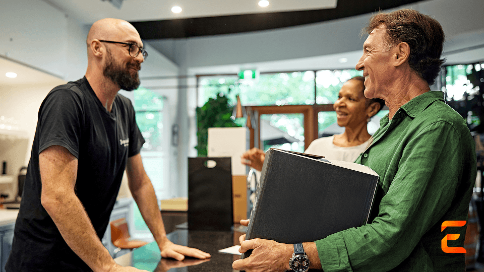 A staff member talks to a smiling couple, the man holding a black box.