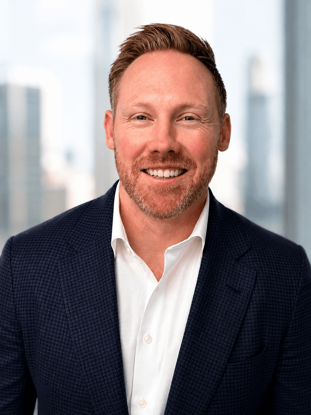 Headshot of a smiling man with a reddish beard in a dark suit jacket.